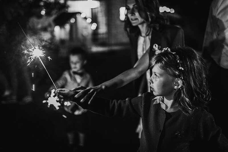 dievča v záblesku svetla, nočná ulica s bokeh svetlami, dieťa s prskavkou, čiernobiela nočná scéna, skupinová oslava vonku, dievča s prekvapeným výrazom. Hotel Zlatý Kľúčik, Nitra.