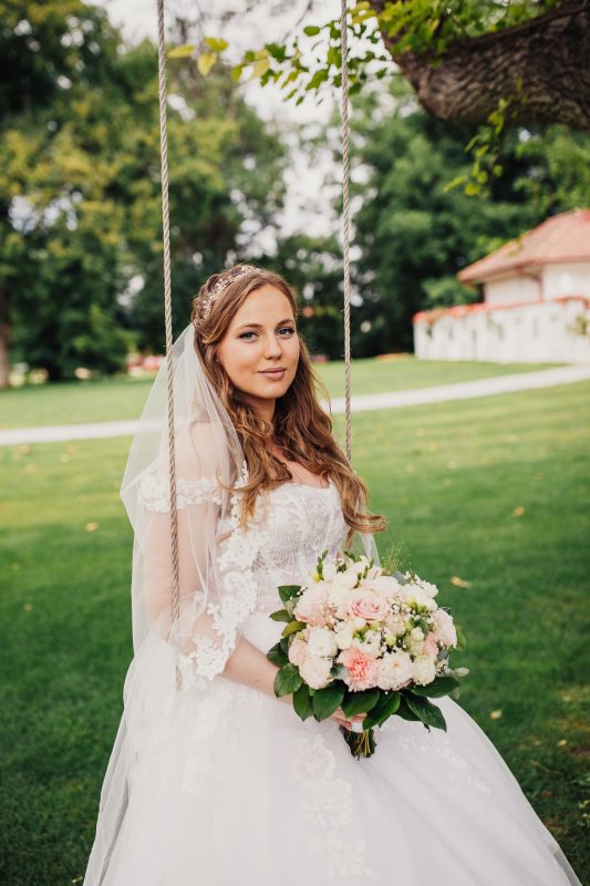 nevesta na hojdačke, svadobné kytice s ružami, čipkované svadobné šaty, nevesta so závojom, slnečný záhradný deň, prírodné svetlo v parku. Art Hotel Kaštieľ Tomášov.