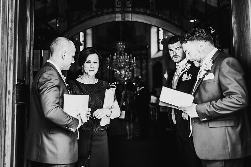 muži v oblekoch s kvetinami, žena v čiernych šatách, čítanie sobášnych listín, elegantný interiér s lustrom, formálna ceremónia v noci. Kaštieľ Villa Bork, Borčice.