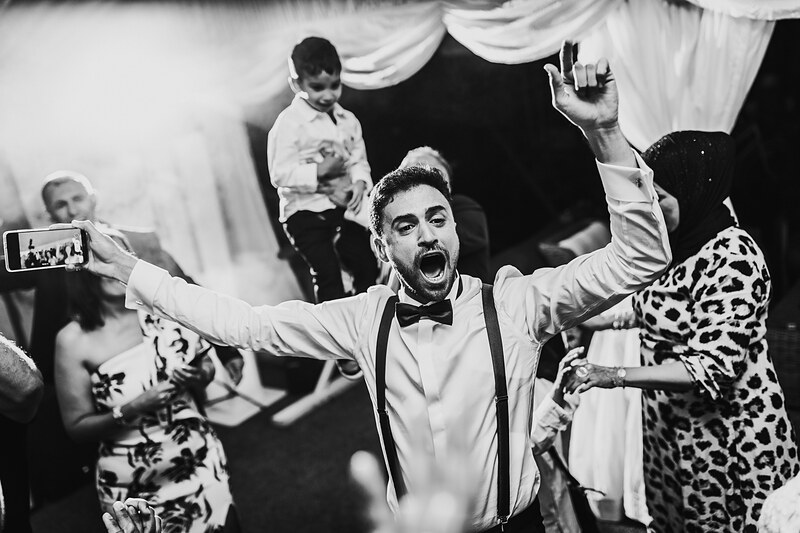 ženích tancuje s radosťou, svadobný tanec v stane, muž v bielej košeli a motýliku, hostia tancujú okolo, čiernobiela svadobná slávnosť, radostná atmosféra na svadbe. Fatima, Trenčín.