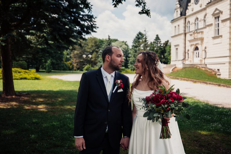 nevesta s červenou kyticou, ženích v čiernom obleku, pár pred klasicistným palácom, slnečný deň v parku, mladomanželia sa pozerajú, zelený trávnik so stromami. Agropenzión Hubert, Ružindol.